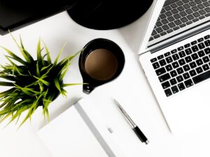 Mesa com vaso de planta, caderno, caneta, caneca e um notebook